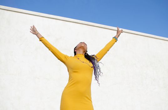 Woman in a vibrant yellow dress expressing joy outdoors against a blue sky.